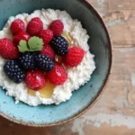 A bowl of creamy cottage cheese topped with fresh berries and honey, served on a rustic wooden table.